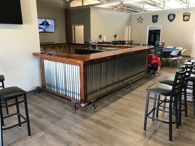 wraparound bar with foot rail, dining table, and flat screen TV and FOP/Police logo on wall